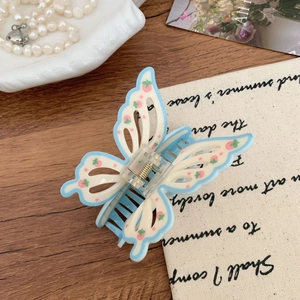 Detail view of a blue and white butterfly hair claw clip with strawberry print and gold spring
