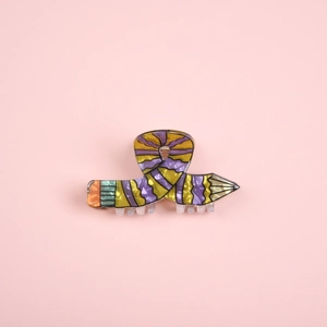 Close-up of a creative pencil-shaped hair claw clip in colorful acetate on pink backdrop