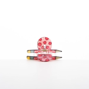 Macro view of a pencil-shaped hair claw clip with red polka dots and metal spring detail