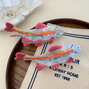 Set of fish-shaped acetate hair claws with colorful translucent patterns on wooden tray