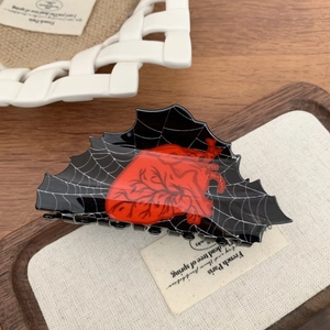 Macro detail of gothic claw clip featuring white spider web patterns and a red heart design