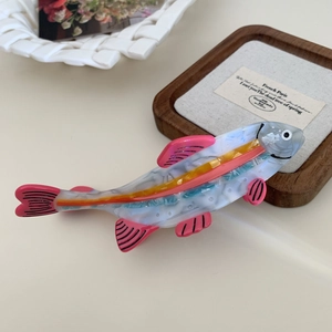 Detailed shot of fish-shaped acetate hair claw clip with marble texture on wooden tray