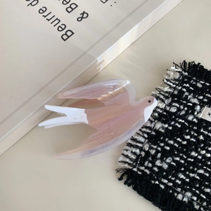 Chic pink acetate swallow hair claw clip displayed on tweed fabric and a white book