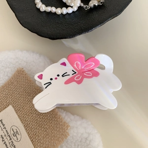 Detail of cute white cat acetate hair claw clip with pink bow on soft sheepskin texture