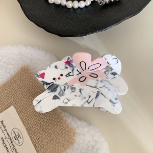 Detail of a cat-shaped acetate hair claw clip with black marble pattern and pink bow accent