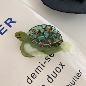 Détail d'une pince à cheveux tortue en acétate vert avec textures dorées sur fond blanc