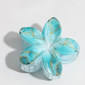 Detail view of blue lily hair claw clip with golden marble patterns on a white background