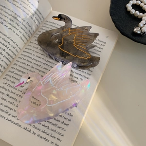 Elegant acetate swan hair claw clips in marble grey and pearly pink on book background