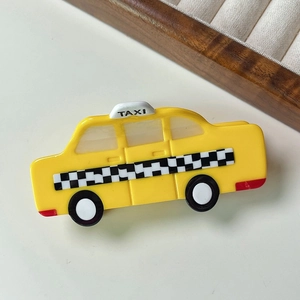 Détail d'une pince à cheveux en acétate en forme de taxi jaune avec motif à damier noir et blanc