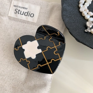 Detail of heart-shaped hair claw with black and white puzzle pattern and gold trim