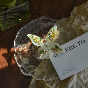 Detailed close-up of a butterfly hair claw with colorful rhinestones on a glass tray