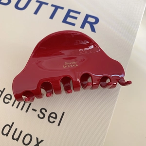Nahaufnahme einer roten Haarspange aus Acetat mit goldener Aufschrift auf strukturiertem Papier