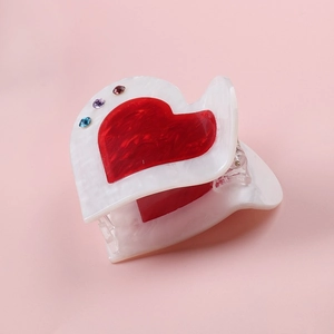 Detail of cream acrylic hair claw with red heart inlay and colorful rhinestones