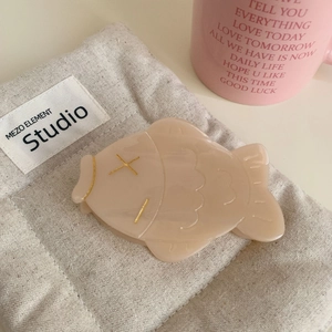 Détail d'une pince à cheveux en acétate crème avec accents dorés et pochon en toile