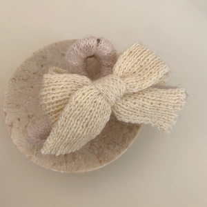 Détail d'une pince à cheveux avec nœud en tricot crème sur un support en pierre texturé