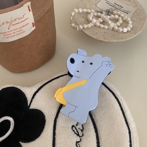 Détail de la pince à cheveux ours bleu clair avec sac jaune posée sur un tapis doux