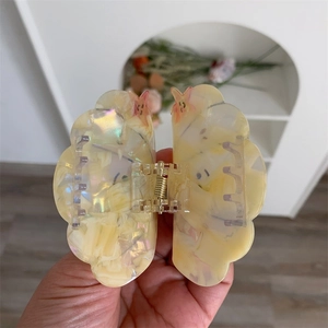 Close-up of a cream yellow cloud-shaped acetate hair claw clip with colorful glitter detail