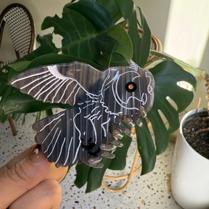 Détail d'une pince à cheveux en forme de hibou en acétate gris foncé avec des lignes peintes