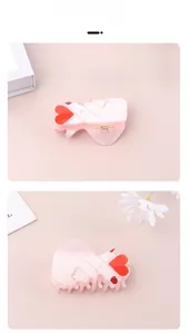 Détail de la pince à cheveux en acrylique rose forme cœur avec strass et ongles rouges