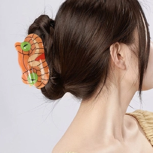Orange snake-shaped acetate hair claw clip with green dots worn in a stylish bun