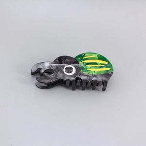 Detail of beetle-shaped hair claw clip with green and yellow marble acetate texture