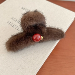 Brown faux fur shark hair clip with a red bead and golden pendant on a book