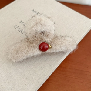 Detailed shot of beige faux fur hair claw clip with red bead and gold charm on book