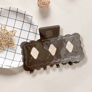 Détail de la pince à cheveux marron foncé motif biscuit avec losanges crème sur le dessus