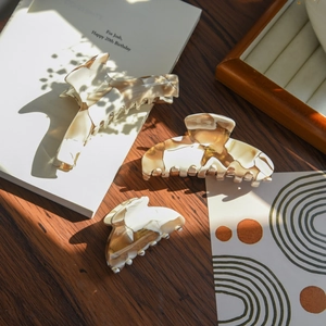 Detailed set of three milk tea marble acetate hair claws on a wooden table with books