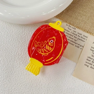 Detailed view of a red lantern claw clip with yellow koi fish pattern and tassel décor