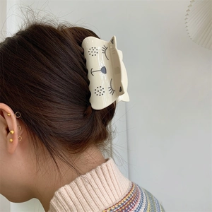 Creamy white acetate hair claw clip featuring a cute squinting cartoon cat design
