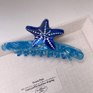 Detailed close-up of blue marble acetate starfish hair claw clip in a linen box
