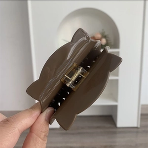 Detail of glossy brown cat-ear hair claw clip with golden metal spring mechanism