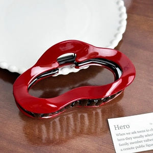 Macro detail of glossy red wave hair claw clip with black teeth on a wooden table