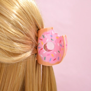 Gros plan d'une pince à cheveux beignet rose avec pépites sur cheveux blonds