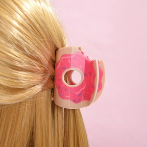 Détail d'une pince à cheveux en forme de donut rose sur des cheveux blonds