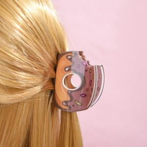 Pince à cheveux motif donut au chocolat sur cheveux blonds avec fond rose pastel doux