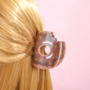 Détail d'une pince à cheveux donut au chocolat avec pépites colorées sur longs cheveux blonds