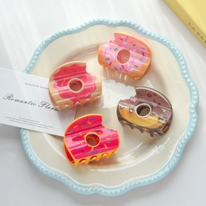 Détail de quatre pinces à cheveux en forme de donuts colorés posées sur une assiette