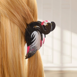 Detail of dark acrylic flamingo hair claw clip styled on blonde hair in soft indoor light