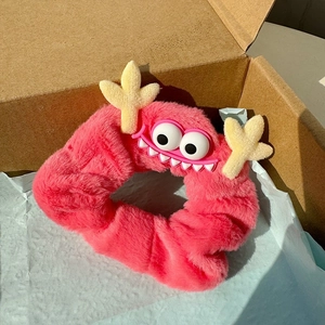 Chouchou monstre en peluche rose avec de grands yeux blancs et des cornes jaunes