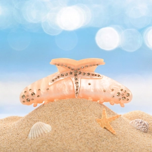 Close-up of a large starfish-shaped claw clip with rhinestones on a sandy beach setting
