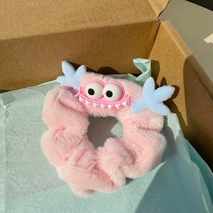 Chouchou monstre en peluche rose avec de grands yeux et des cornes bleues sur papier