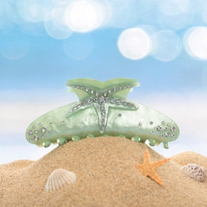Close-up of mint green starfish hair claw clip with rhinestones on a sandy beach