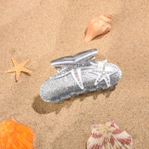 Gros plan d'une pince à cheveux étoile de mer argentée avec strass sur plage de sable