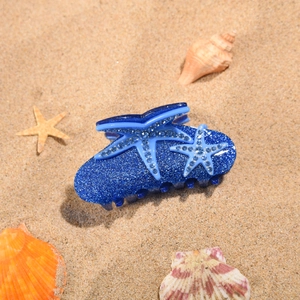 Détail de la pince à cheveux étoile de mer bleue avec strass sur un fond de sable de plage