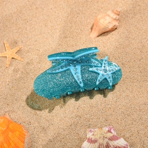 Détail de la pince à cheveux étoile de mer bleue avec strass sur plage de sable