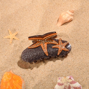 Gros plan d'une pince à cheveux étoile de mer avec strass brillants sur le sable