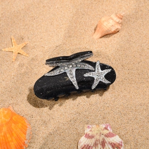 Détail d'une grande pince à cheveux noire avec étoiles de mer en strass sur sable de mer