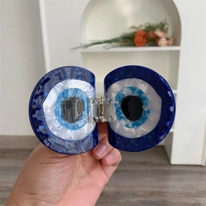 Detailed view of evil eye patterned acetate hair claw clip with blue iris and brand logo